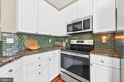 a kitchen with granite countertop white cabinets stainless steel appliances and wooden floor