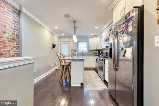 a kitchen with stainless steel appliances granite countertop a refrigerator a sink a stove and white cabinets with wooden floor