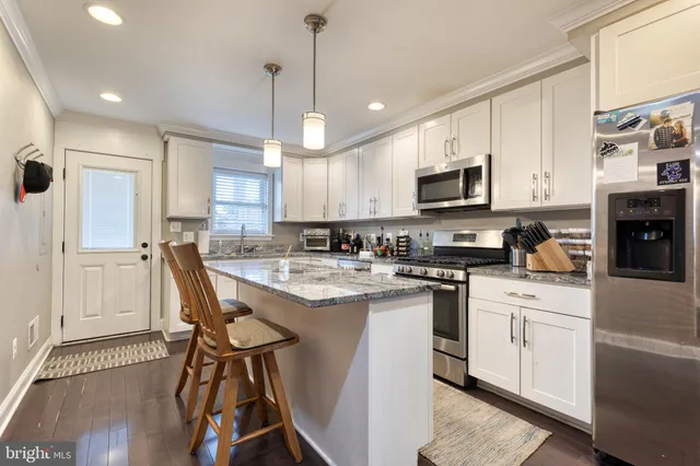 a kitchen with stainless steel appliances granite countertop a stove top oven a refrigerator a sink and white cabinets with wooden floor