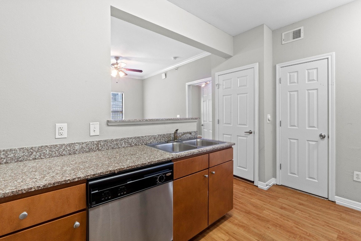 2502 Leon Street, Unit 213 Austin, TX 78705 - Photo 8 of 20 Kitchen featuring stainless steel dishwasher, brown cabinets, a peninsula, light wood-style flooring, and ornamental molding