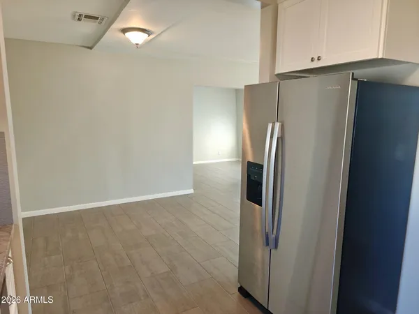 a view of a refrigerator in kitchen and an empty room with wooden floor