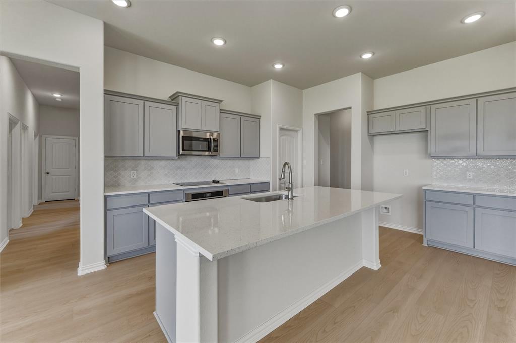 114 Hillview Trail Decatur, TX 76234 - Photo 8 of 27 Contemporary kitchen featuring a large central island with a sink, light gray cabinetry, stainless steel microwave, white countertops, and a patterned backsplash