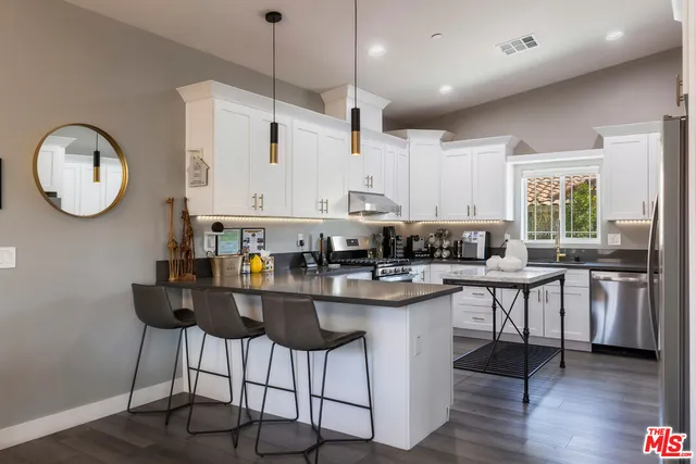 a kitchen with stainless steel appliances granite countertop a sink a stove a refrigerator and island with wooden floor