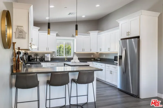 a kitchen with stainless steel appliances a table a stove a refrigerator a kitchen island a dining table and chairs with wooden floor