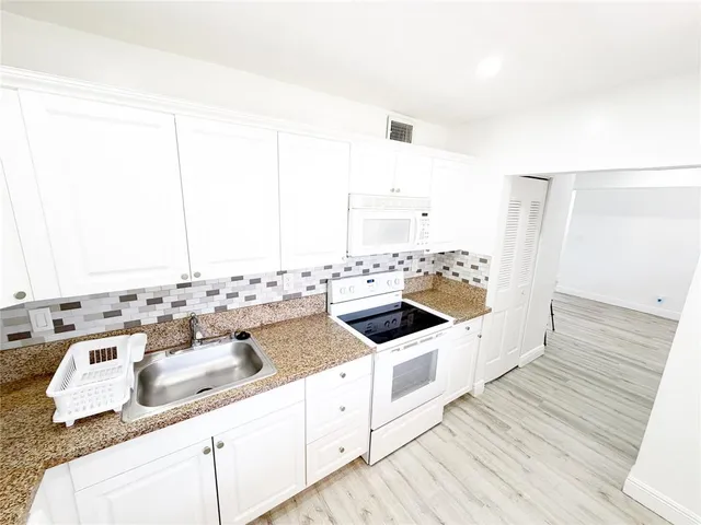 a kitchen with a sink and white cabinets with wooden floor
