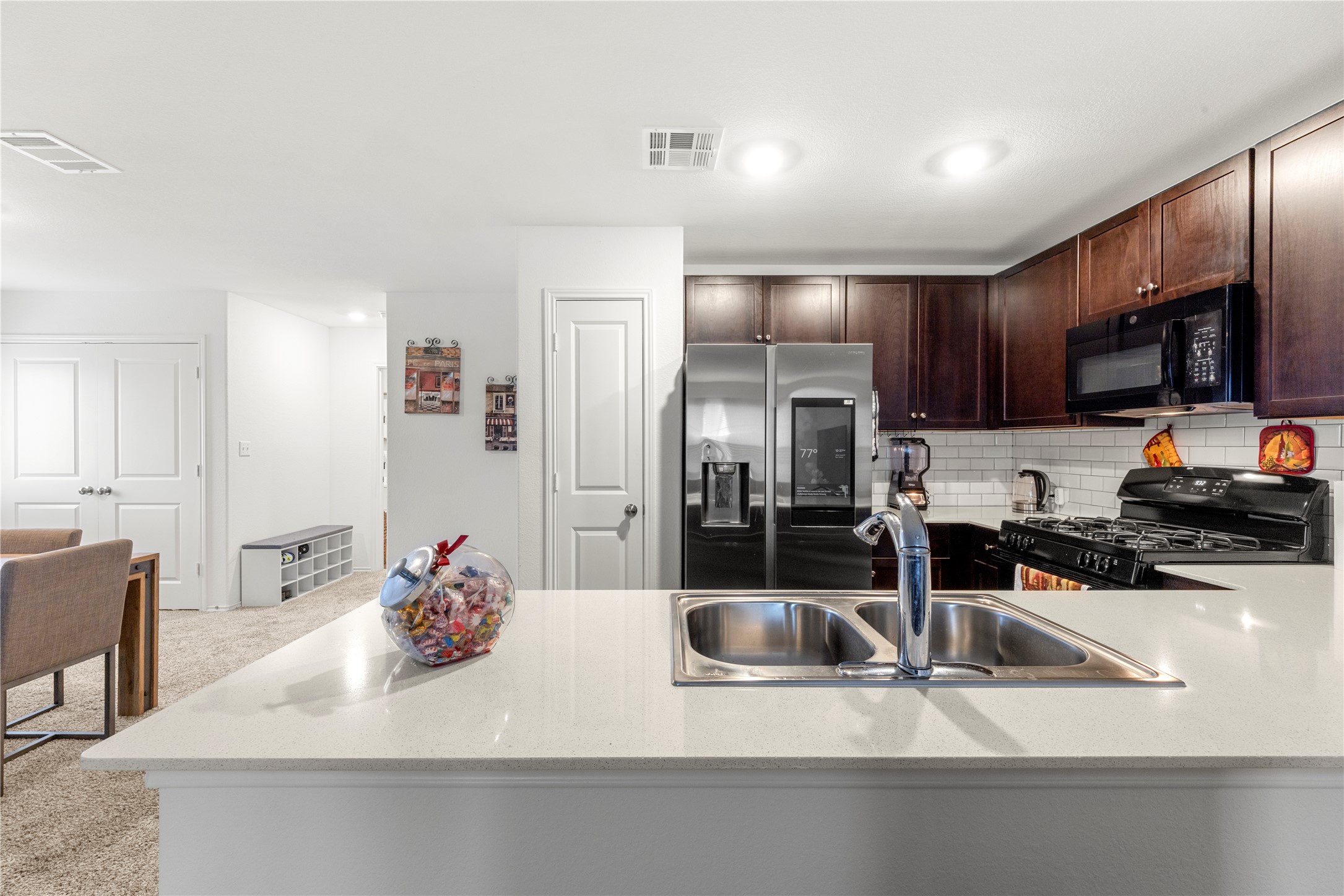 17701 Oso Cove Elgin, TX 78621 - Photo 3 of 9 Kitchen with dark wood finish cabinets, black appliances, a peninsula, light colored carpet, and backsplash