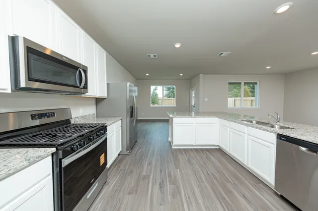 a kitchen with stainless steel appliances kitchen island granite countertop wooden cabinets stove top oven and sink