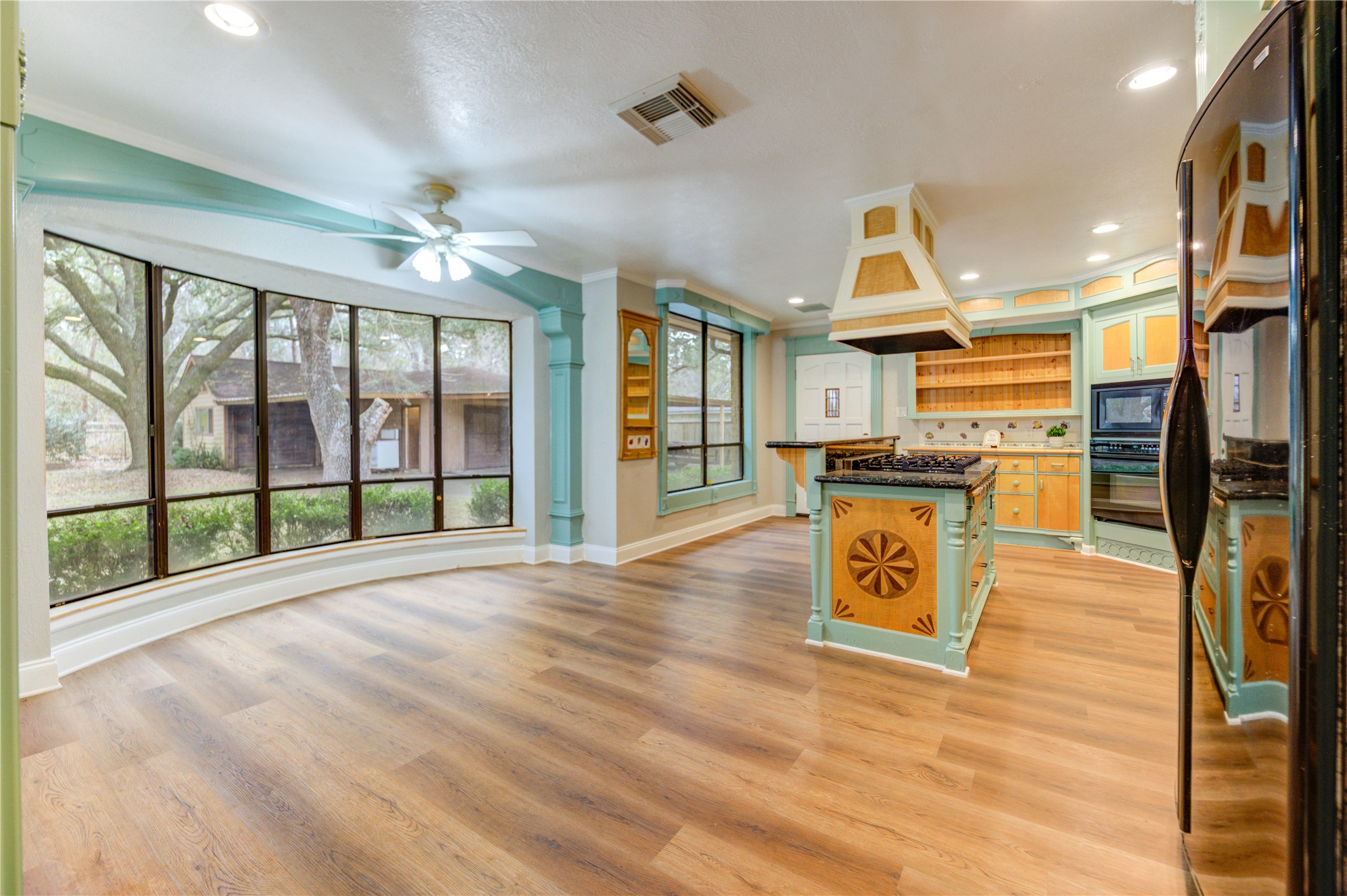 24316 East Webb Road Porter, TX 77365 - Photo 6 of 14 This spacious kitchen features large windows with a beautiful garden view, vibrant cabinetry, and a central island with a unique hood design. The open layout and wood flooring create a warm, inviting atmosphere perfect for cooking and entertaining.