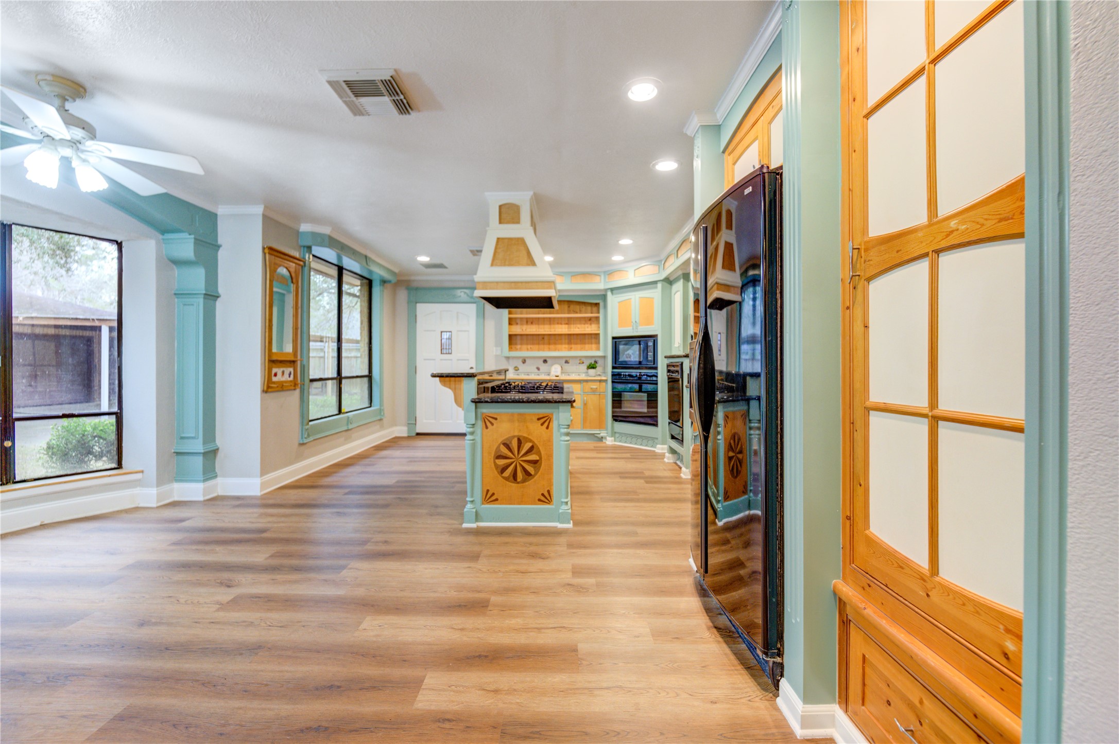 24316 East Webb Road Porter, TX 77365 - Photo 8 of 14 This bright kitchen features unique, colorful cabinetry with decorative accents and ample natural light from large windows. It includes modern appliances, a ceiling fan, and a cozy breakfast nook, all set on stylish hardwood flooring.