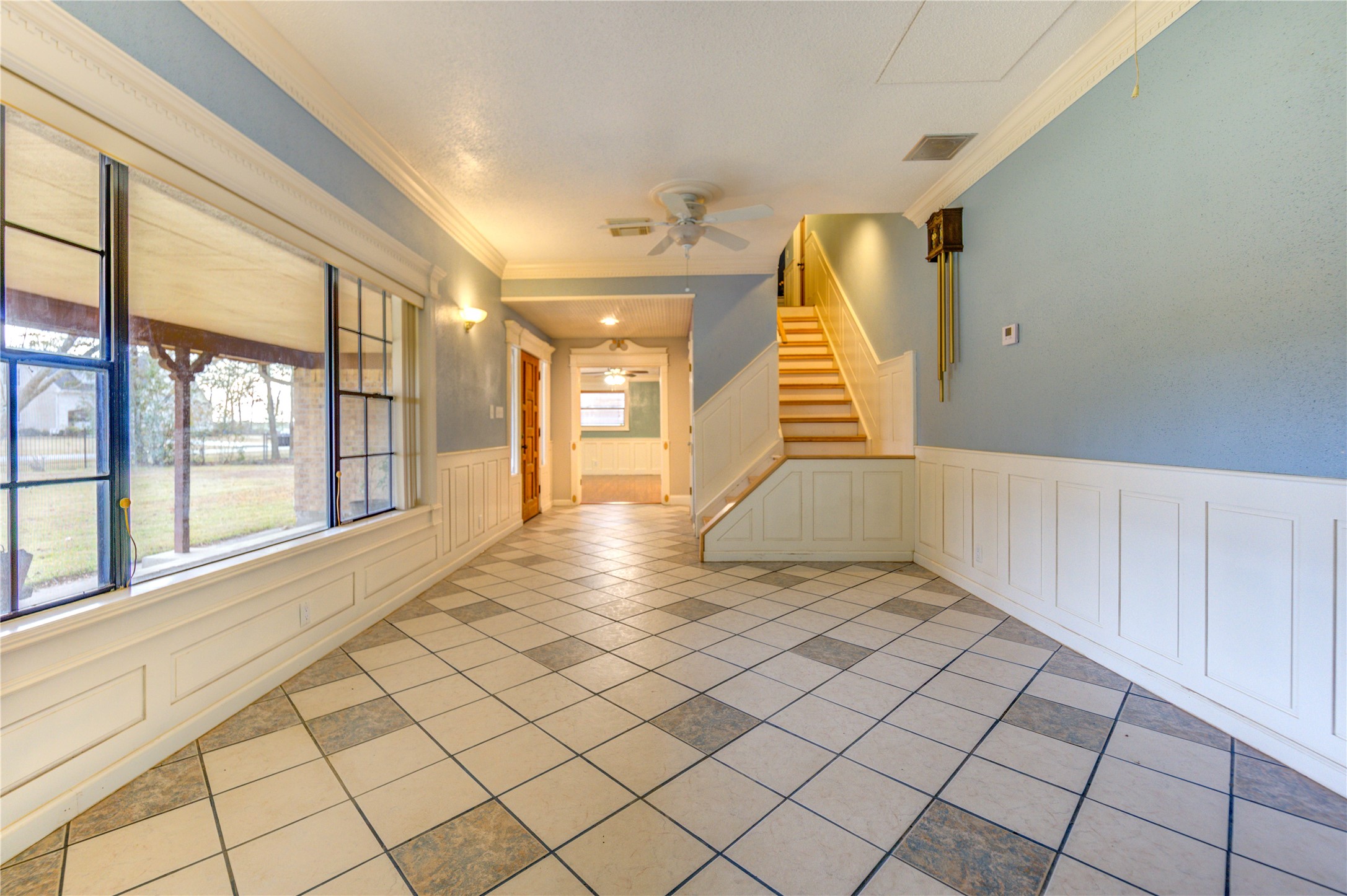 24316 East Webb Road Porter, TX 77365 - Photo 10 of 14 This inviting space features a tiled floor with a mix of square patterns, soft blue walls, and wainscoting. A large window provides ample natural light, while a staircase leads to the upper level.
