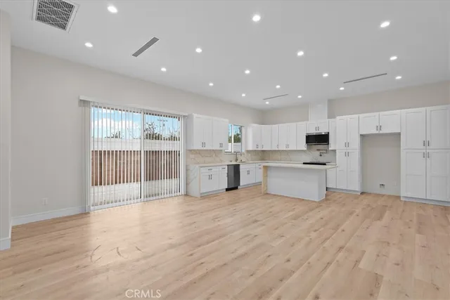 a large kitchen with stainless steel appliances a sink dishwasher a refrigerator and white cabinets with wooden floor