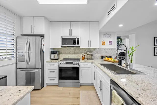 a kitchen with stainless steel appliances granite countertop a refrigerator a stove a sink a microwave a refrigerator and white cabinets with wooden floor