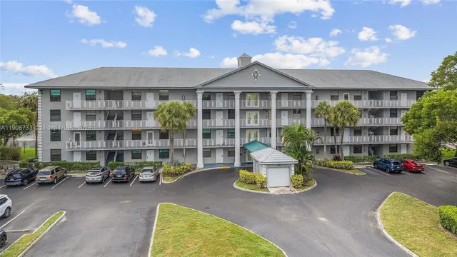 a view of a building with large trees and cars parked in front of it