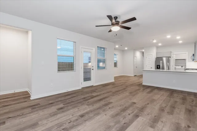 a view of an empty room with wooden floor and a kitchen