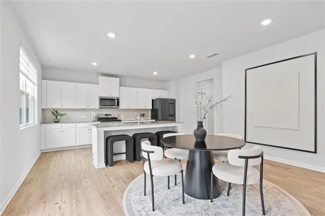 a open kitchen with white cabinets a sink dishwasher a dining table and chairs with wooden floor