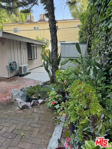 a pathway of a house with potted plants and a bench