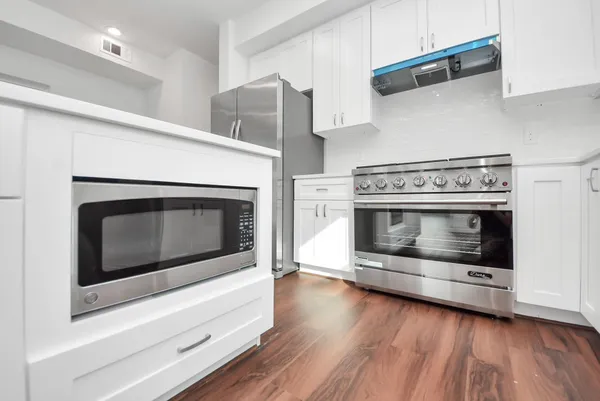 a kitchen with granite countertop a stove a refrigerator and a white cabinets