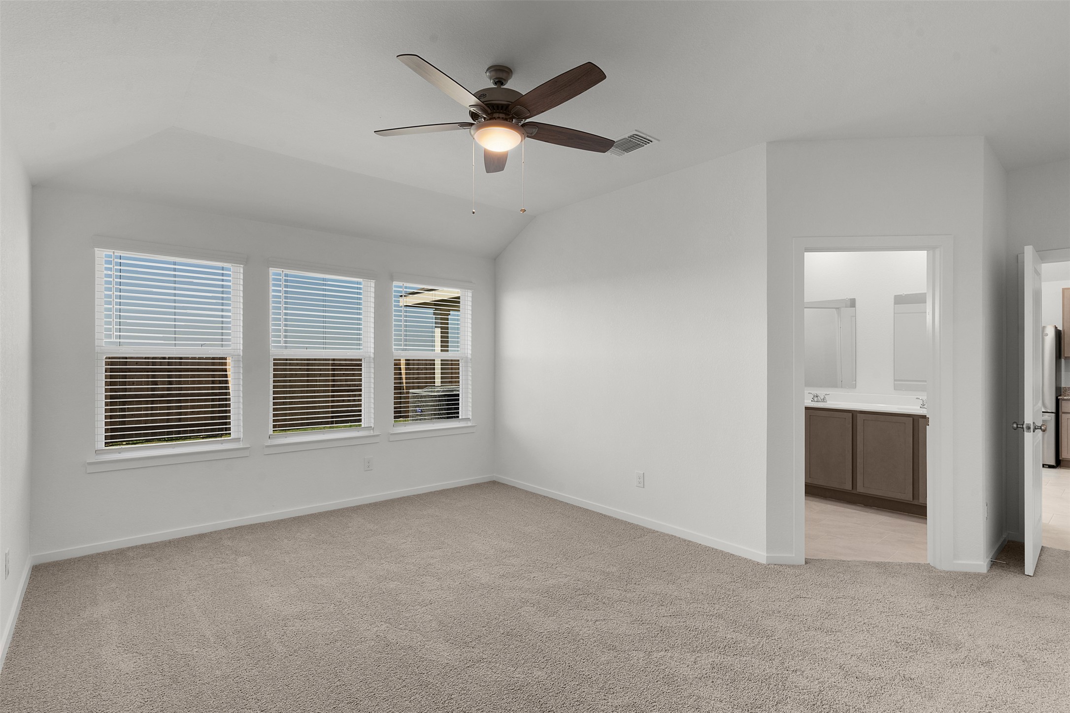 13832 Scarlett Song Drive Elgin, TX 78621 - Photo 12 of 26 Unfurnished bedroom featuring light colored carpet, a ceiling fan, vaulted ceiling, ensuite bathroom, and freestanding refrigerator