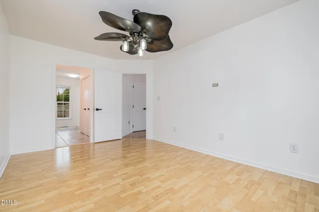 an empty room with a chandelier fan and wooden floor