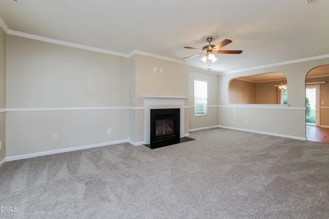 a view of an empty room with chandelier fan and fire place