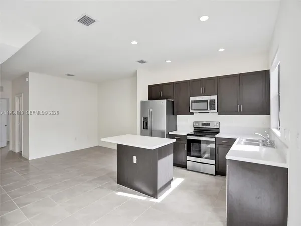 a kitchen with stainless steel appliances a stove top oven a sink a refrigerator and white cabinets