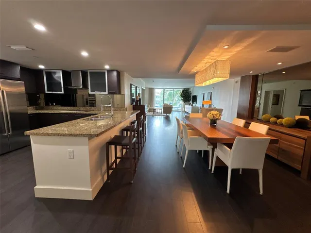 a large dining hall with stainless steel appliances granite countertop a stove a sink a dining table and chairs with wooden floor