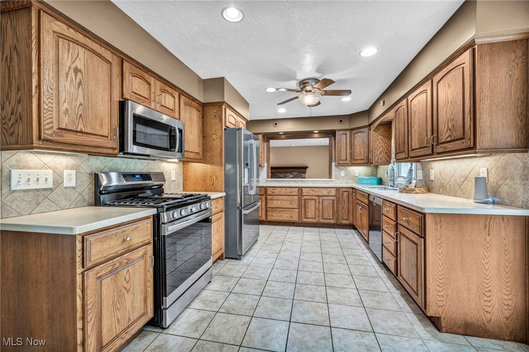 38814 Johnnycake Ridge Road Willoughby, OH 44094 - Photo 17 of 48 Kitchen featuring appliances with stainless steel finishes, ceiling fan, tasteful backsplash, brown cabinetry, and recessed lighting