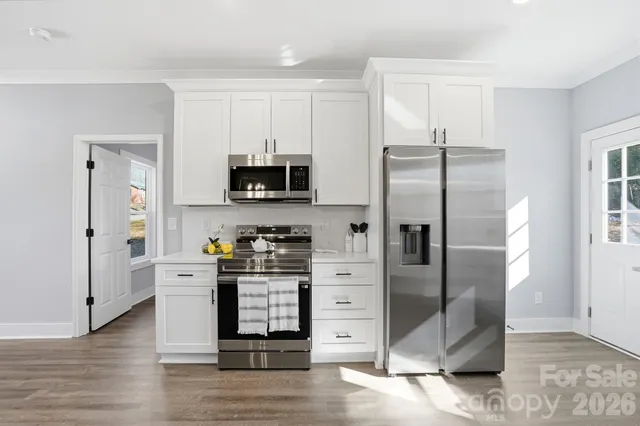 a kitchen with stainless steel appliances granite countertop a refrigerator a stove a sink and white cabinets