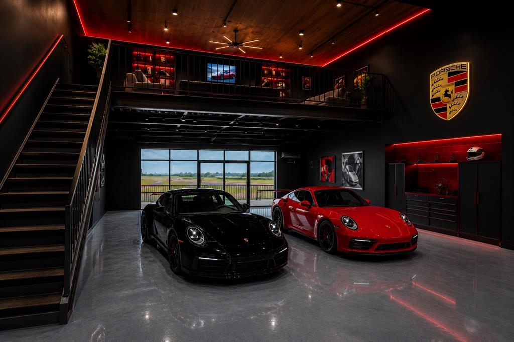 Automotive storage space featuring a polished concrete floor, overhead loft with metal railing, and expansive glass roll-up door