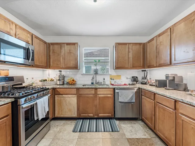 a kitchen with stainless steel appliances granite countertop a stove a sink dishwasher and a microwave oven with wooden cabinets