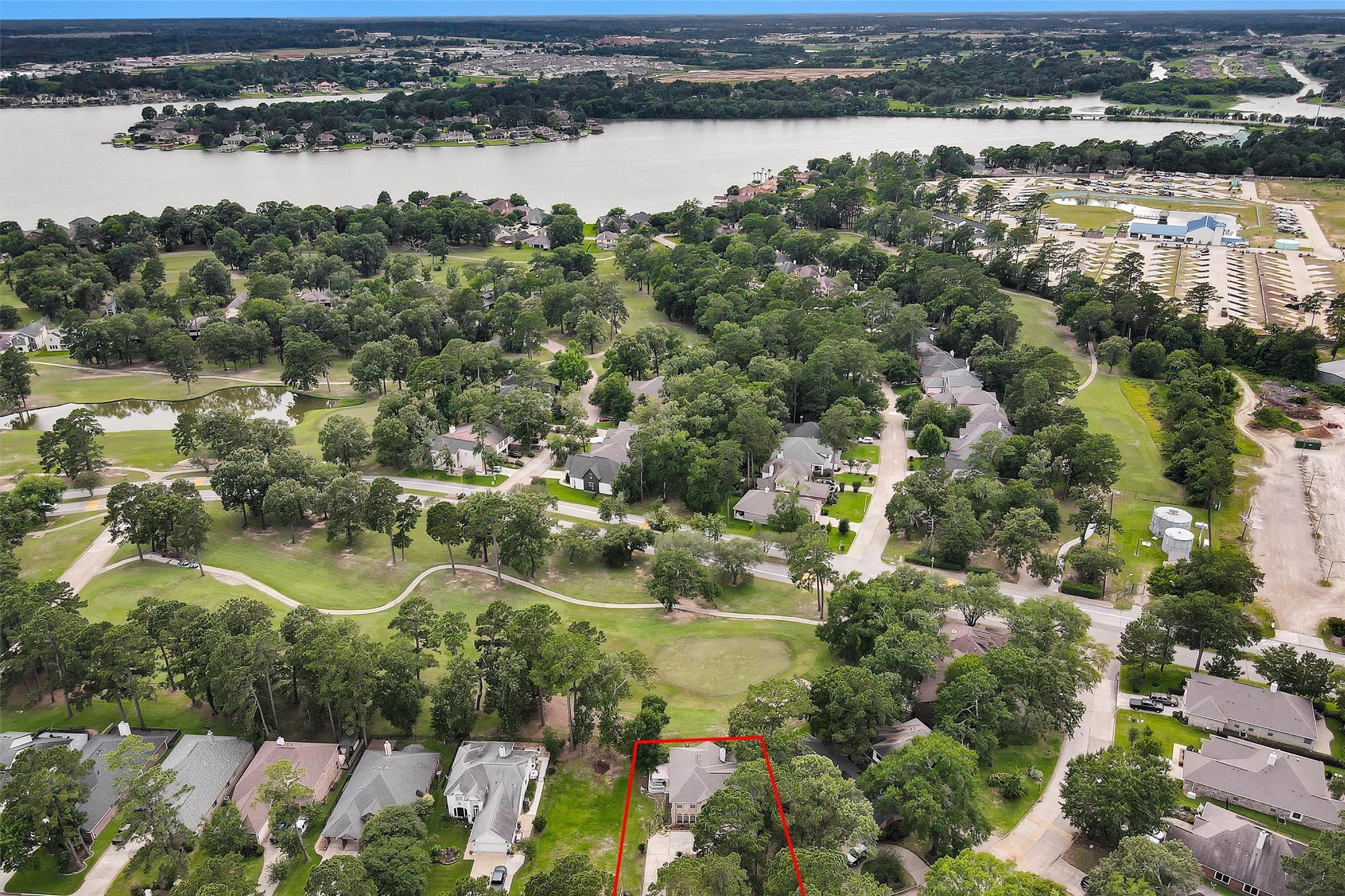 23 Alba Road Montgomery, TX 77356 - Photo 1 of 37 This aerial photo shows a house outlined in red, nestled in a lush, green neighborhood. The area features spacious lots with mature trees and is close to a large body of water, providing a serene setting. Nearby, there are other well-maintained homes and open green spaces, creating a peaceful residential atmosphere.