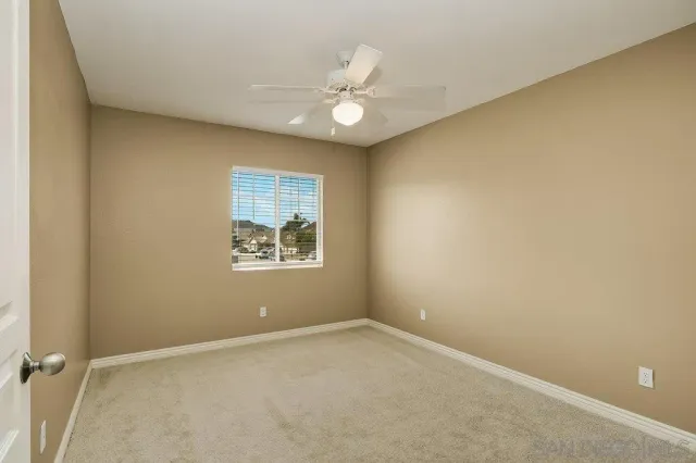 an empty room with a chandelier fan and windows