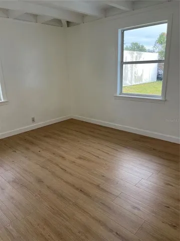 a view of an empty room with wooden floor and a window