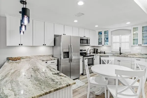 a kitchen with stainless steel appliances granite countertop a refrigerator a stove a sink a dining table and chairs