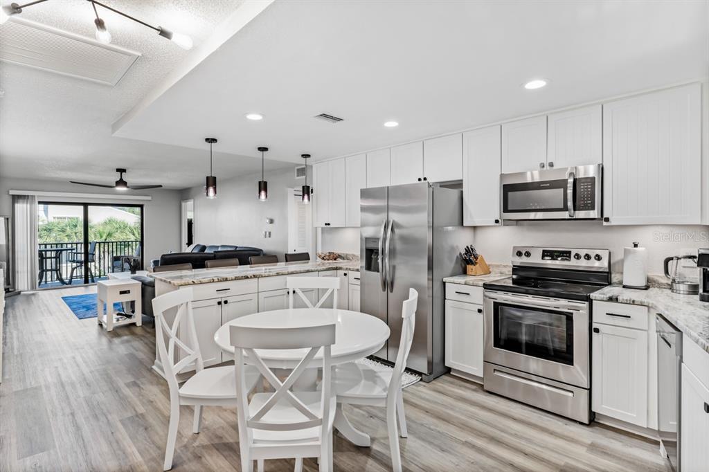3210 Gulf Boulevard, Unit 307 Belleair Beach, FL 33786 - Photo 13 of 44 a kitchen with a refrigerator a stove top oven a sink dishwasher a dining table and chairs with wooden floor
