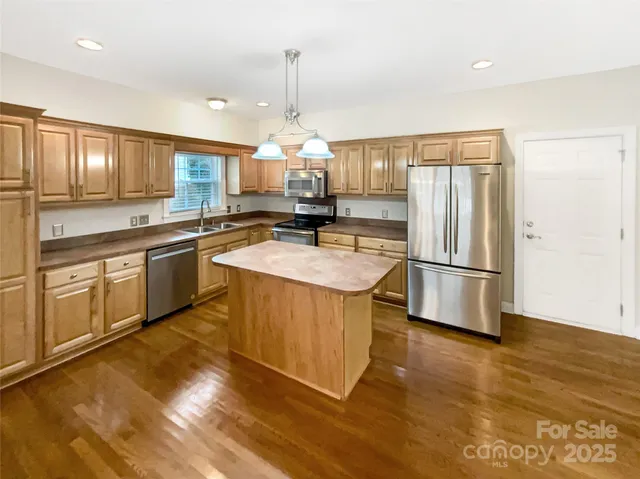 a kitchen with stainless steel appliances granite countertop a sink a stove a refrigerator and island with wooden floor