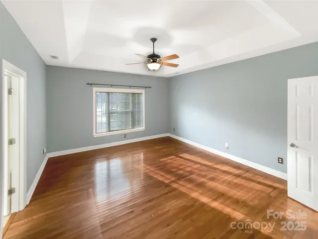 an empty room with wooden floor ceiling fan and windows