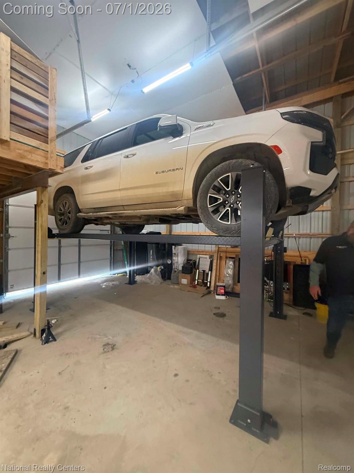 1330 Brauer Road Oxford, MI 48371 - Photo 27 of 54 Spacious garage with a four-post vehicle lift, concrete flooring, exposed wood beam ceiling, fluorescent lighting, and a large roll-up door