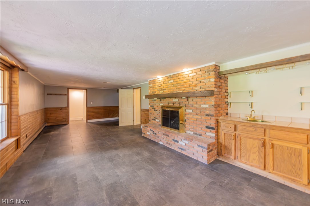 7969 Dines Road Novelty, OH 44072 - Photo 35 of 48 Spacious family room featuring a brick fireplace with a wood mantle, wood-finish flooring, wood paneling, a built-in wet bar with cabinetry, and a window with wood trim