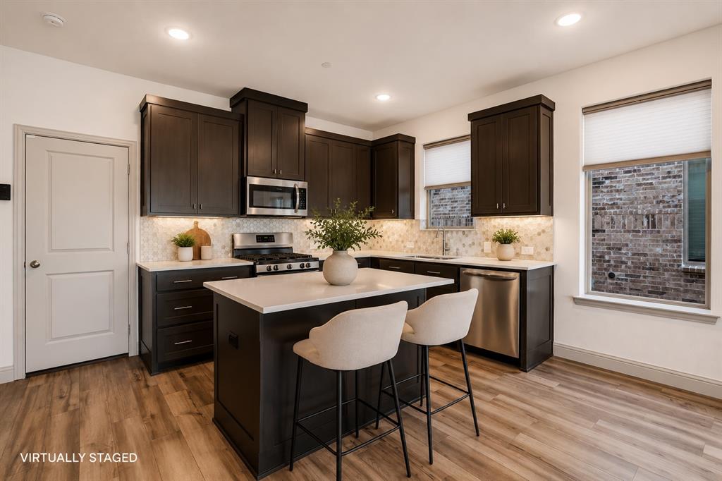 421 Matchbox Street Argyle, TX 76226 - Photo 7 of 40 Modern kitchen featuring dark wood cabinetry, stainless steel appliances, a white stone countertop island with seating, patterned tile backsplash, and wood-finish flooring