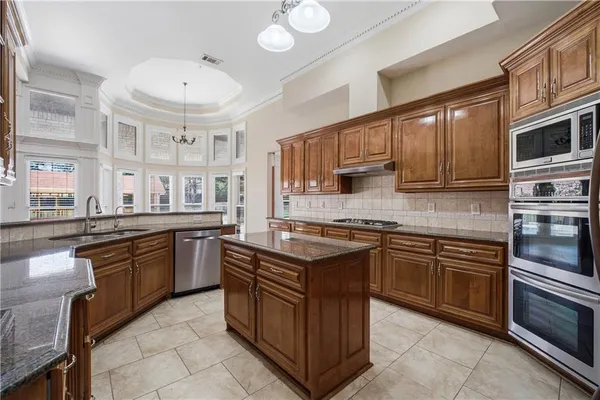 a kitchen with stainless steel appliances granite countertop a stove top oven a sink dishwasher a dining table and chairs with wooden cabinets