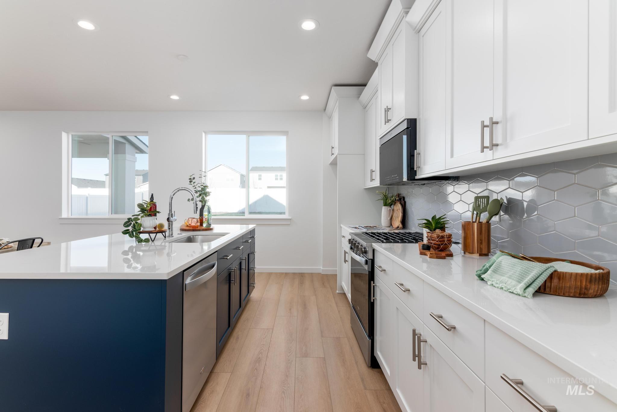 8409 South Wavecrest Avenue Kuna, ID 83634 - Photo 6 of 12 Kitchen with two tone color scheme, stainless steel appliances, light stone counters, an island with sink, and light wood finished floors