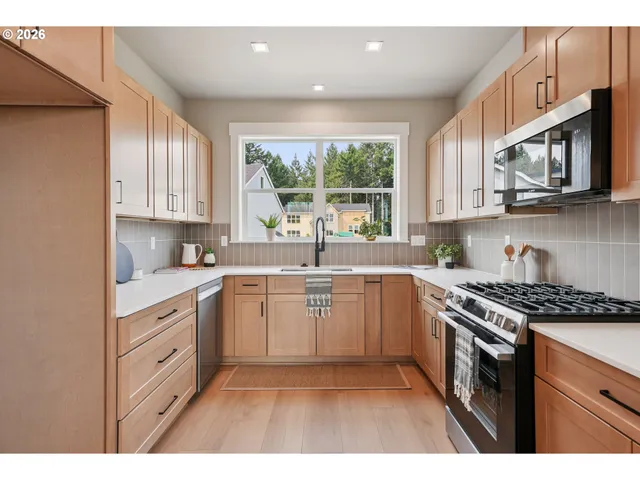 a kitchen with stainless steel appliances granite countertop a sink a stove a microwave cabinets and a window