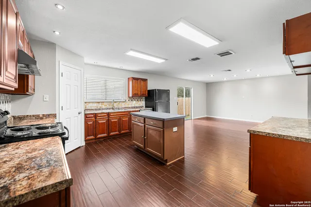 a kitchen with granite countertop a stove top oven a sink dishwasher and a refrigerator with wooden floor