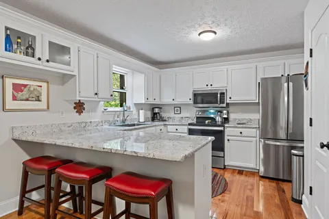 a kitchen with stainless steel appliances granite countertop a dining table chairs refrigerator and sink