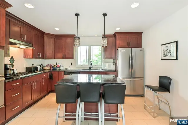 a kitchen with stainless steel appliances granite countertop a dining table chairs refrigerator and sink