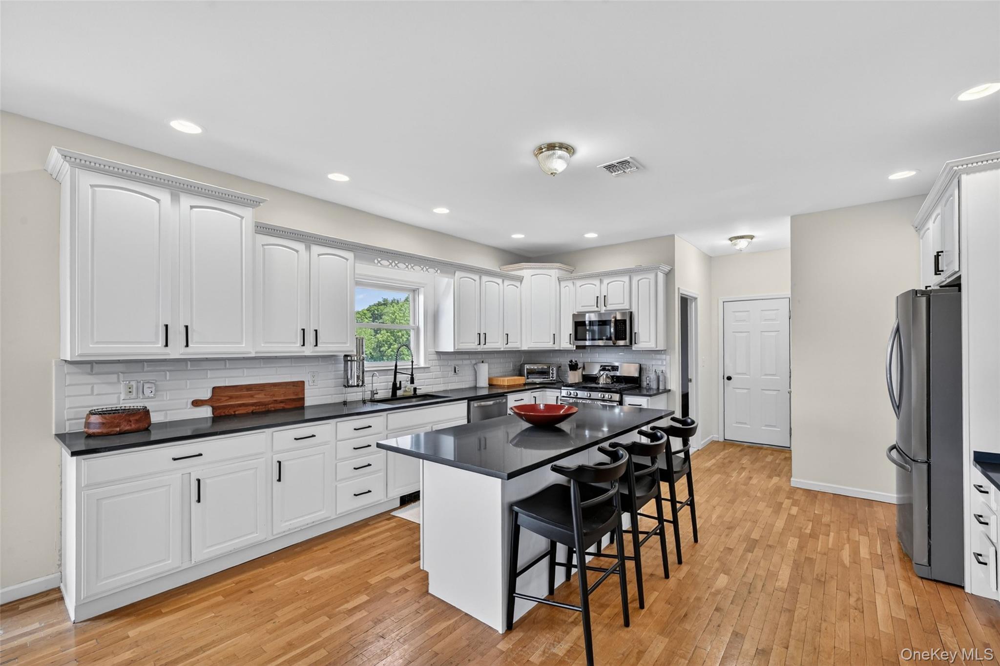 19 Bull Mine Road Chester, NY 10918 - Photo 13 of 42 Kitchen featuring a central island with countertop seating, white shaker-style cabinetry with crown molding, dark countertops, subway tile backsplash, and light wood-finish flooring