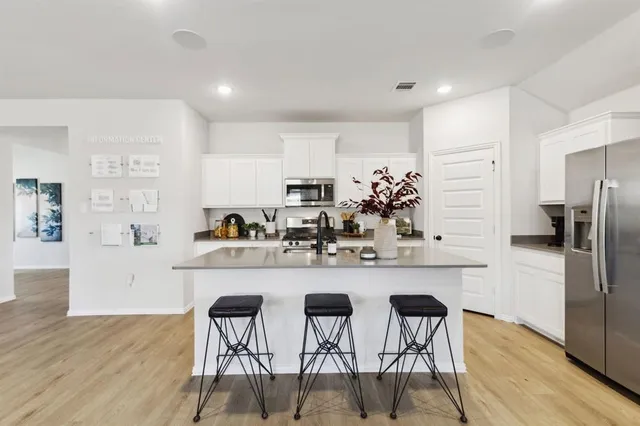 a kitchen with stainless steel appliances a dining table chairs refrigerator and cabinets