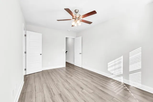 a view of an empty room with wooden floor and a ceiling fan