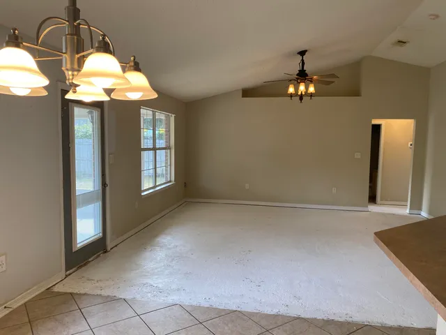 an empty room with chandelier fan and windows